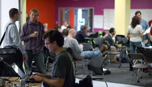 closer image of Jam attendees at tables with laptops, or standing around conversing